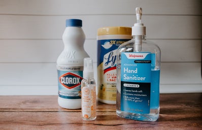 a bottle of clorox, hand sanitizers and a container of lysol wipes sit on a wooden table