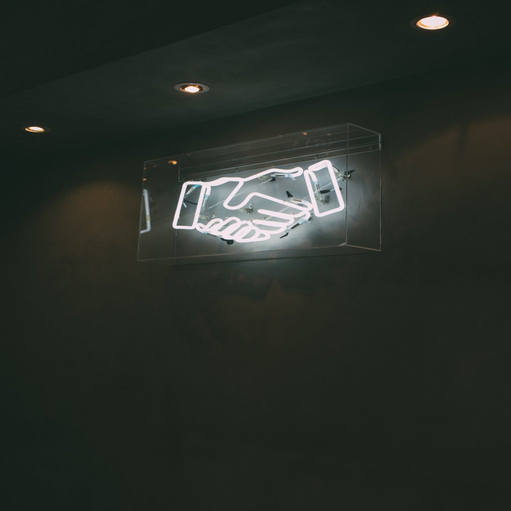 a black and white photo of a neon sign of two hands shaking