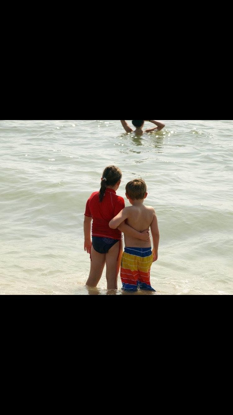A little boy and girl with arms around each other at the beach