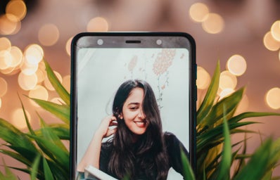 a picture of a picture of a woman on a phone, which is tucked into a plant with fairy lights behind it