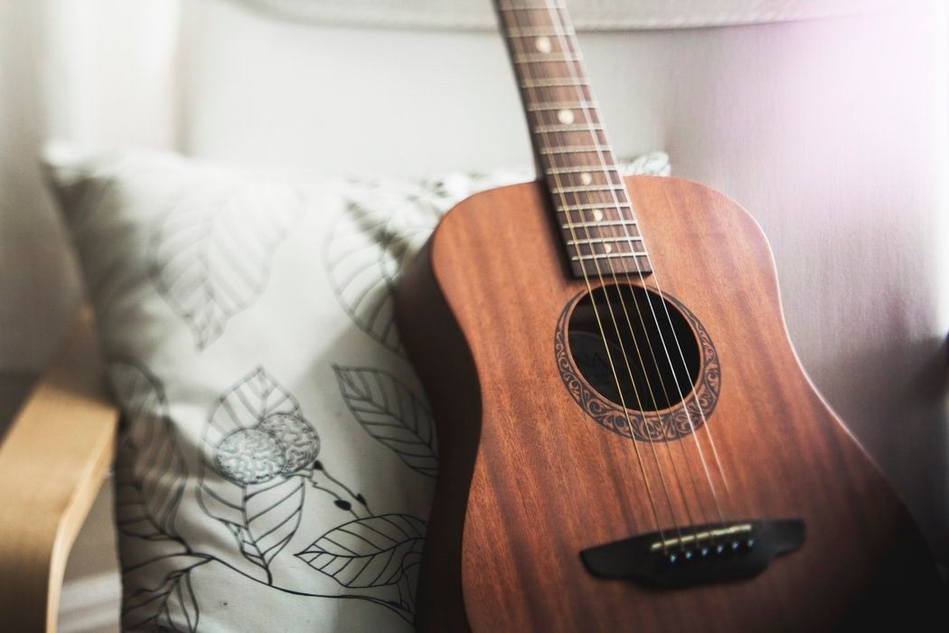 A brown guitar sitting on a white chair with a pillow.