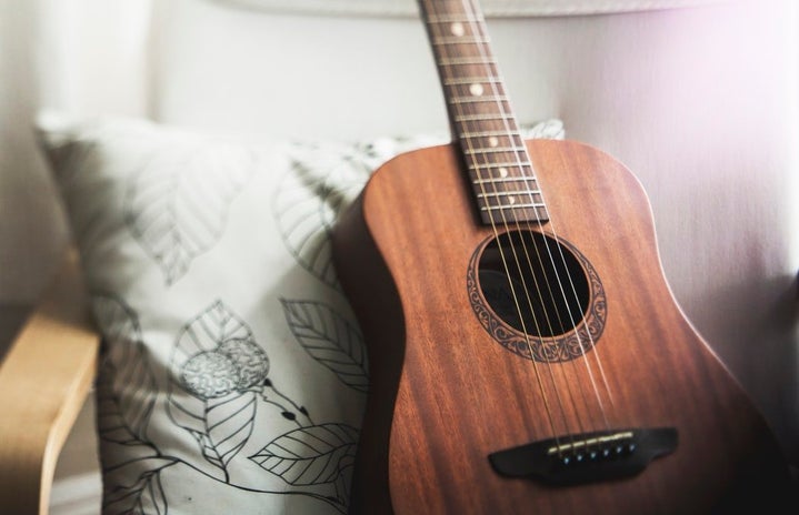 A brown guitar sitting on a white chair with a pillow.