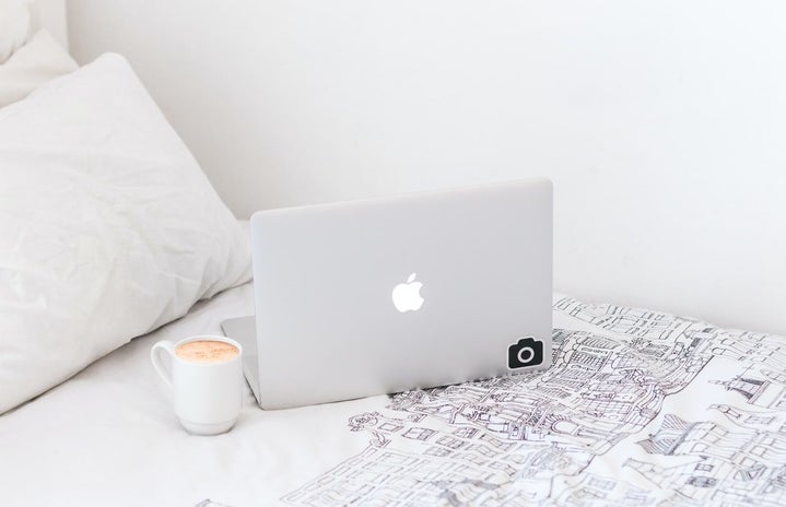 A silver Macbook on a bed next to a cup of coffee