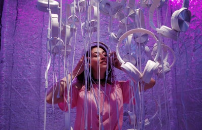 photo of woman wearing pink shirt standing near white headphones against purple background