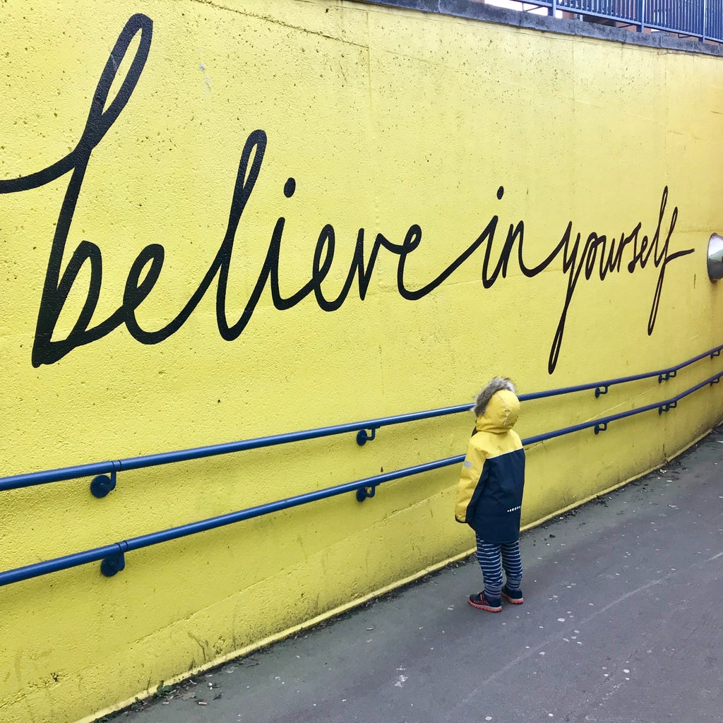child looking up at inspirational quote on a mural