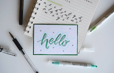 green and white Hello board decor on top of notebook with handwritten lettering framed by brush pens