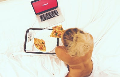 girl watching Netflix while eating pizza in bed