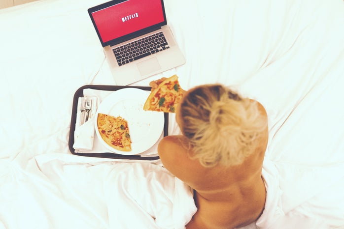 girl watching Netflix while eating pizza in bed