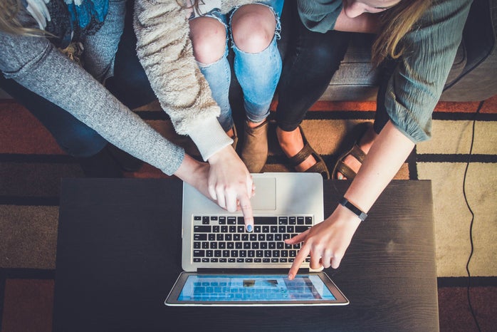 three women pointing at a silver laptop screen