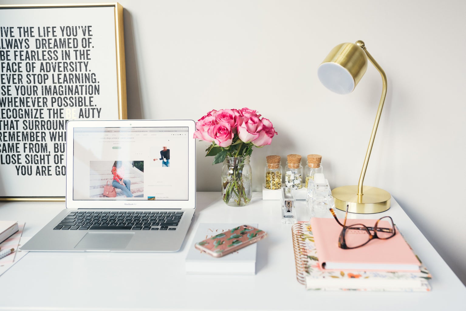 MacBook Air on white desk beside gold-colored study lamp and spiral books