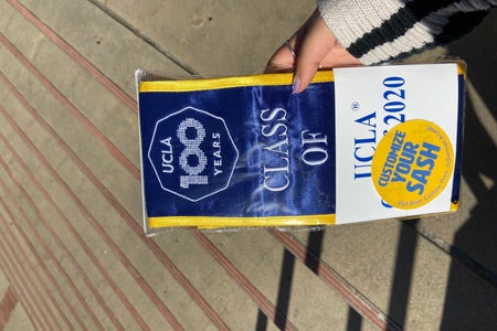 hand holding a ucla class of 2020 sash inside packaging