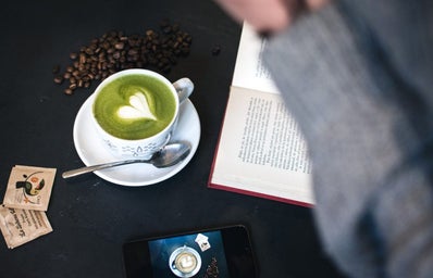 dark cafe desk with phone, matcha latte, and book.