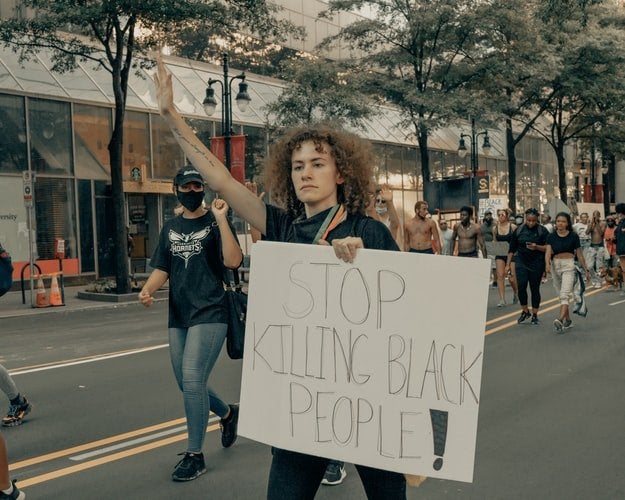 Protester holding sign that says \"stop killing black people\"