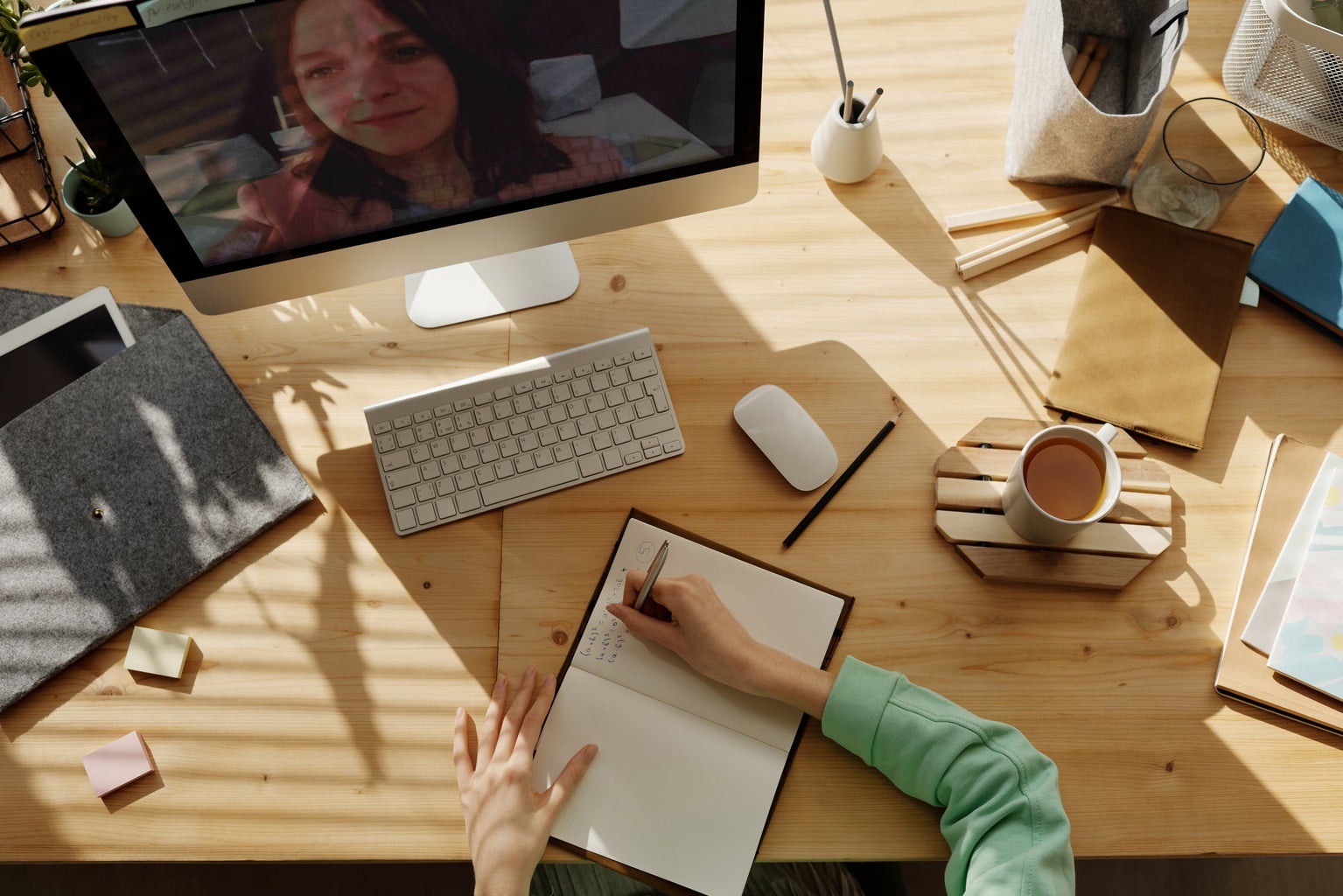 overhead shot of a desk with someone writing in a notebook and on a video call on a computer