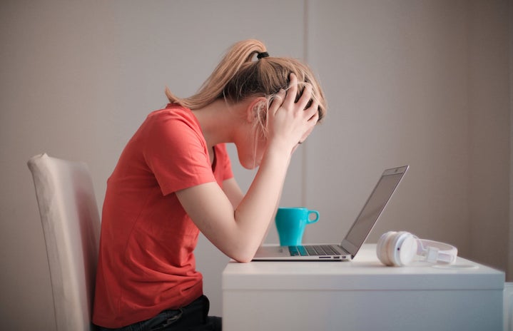 blonde woman with ponytail with her head in her hands leaning over a laptop
