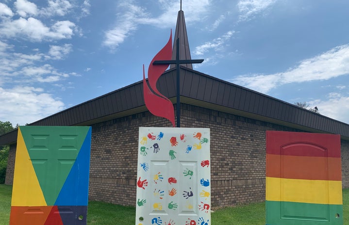 Rainbow painted doors in front of metal cross