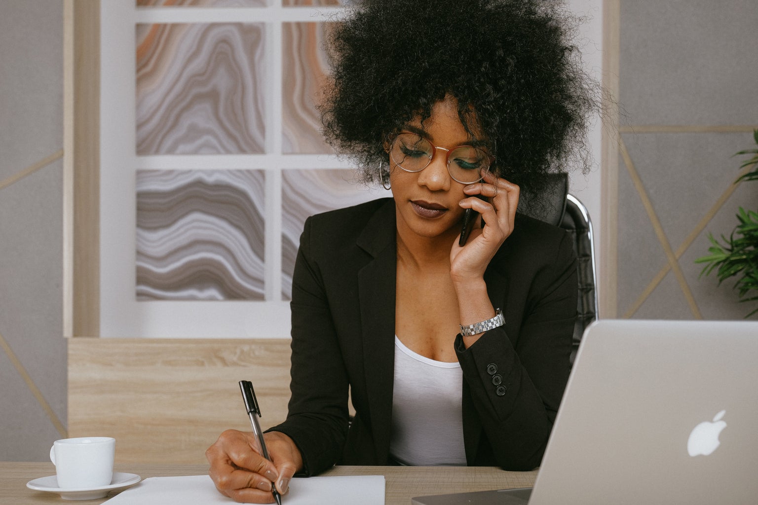 woman in black blazer on the phone taking notes