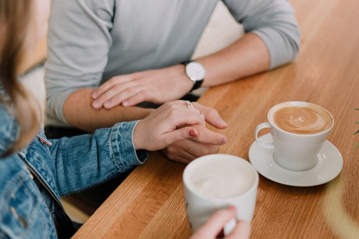 couple holding hands while drinking coffee at table