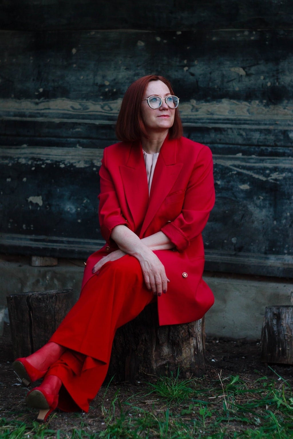 woman in red suit with glasses sitting on tree stump
