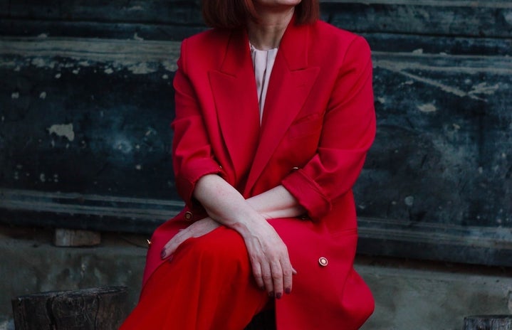 woman in red suit with glasses sitting on tree stump