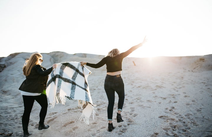 alt="vignette photography of two woman holding scarf walking on sand"
