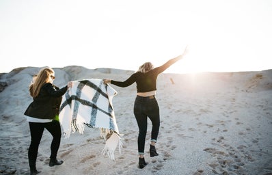 alt=\"vignette photography of two woman holding scarf walking on sand\"