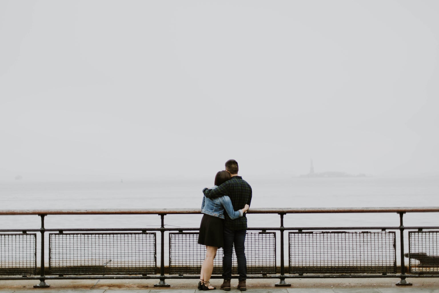 couple standing in front of fence near body of water