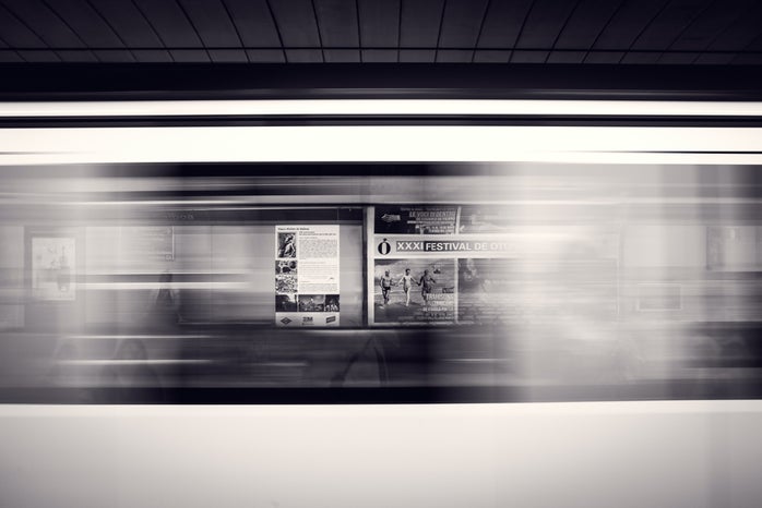 A long-exposure shot of a moving subway train and advertisement posters at the station