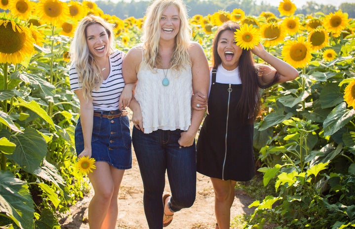 three women standing between sunflowers