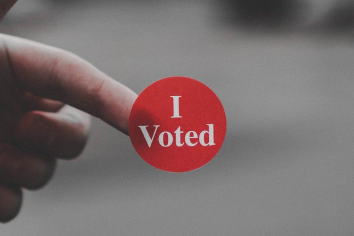 Hand holding a red sticker with the words "I Voted"