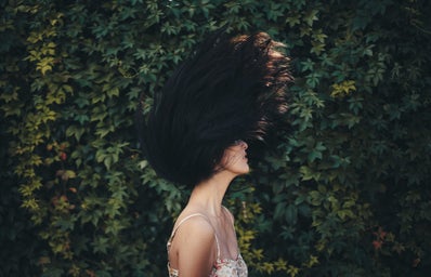 woman waving her hair in front of green leafed wall