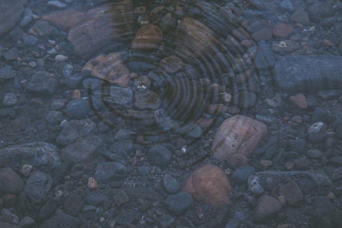 ripple on crystal clear water revealing smooth stones beneath the surface