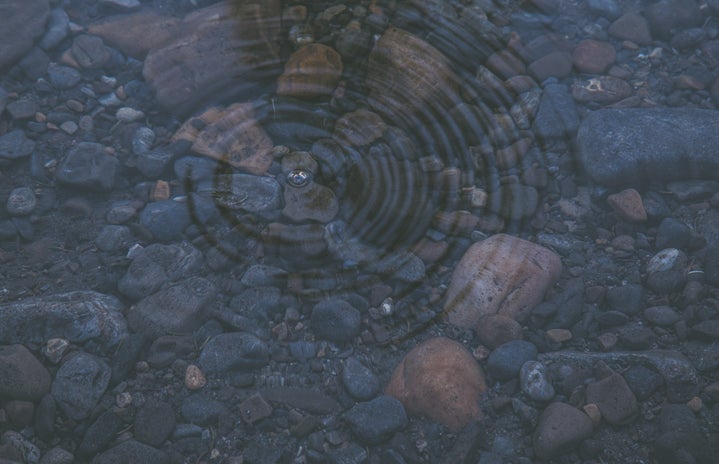 ripple on crystal clear water revealing smooth stones beneath the surface
