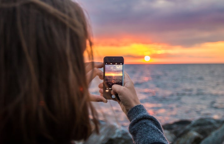 woman holding phone taking a photo of sunset