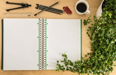 green and white grid notebook on desk with pencils, coffee, and plant