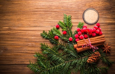 pine leaves, holly, a bundle of cinnamon, and a pinecone on a wooden table