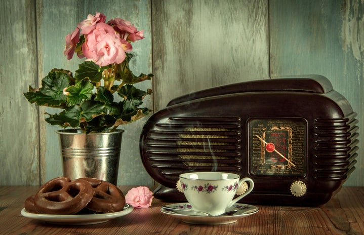 antique radio, pink flowers, pretzels, and tea cup on a wooden table with blue worn wood backdrop