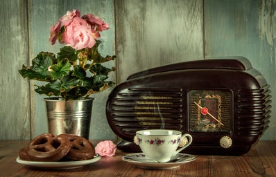antique radio, pink flowers, pretzels, and tea cup on a wooden table with blue worn wood backdrop