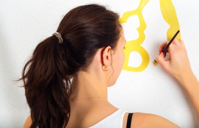 woman painting pattern on white wall with yellow paint