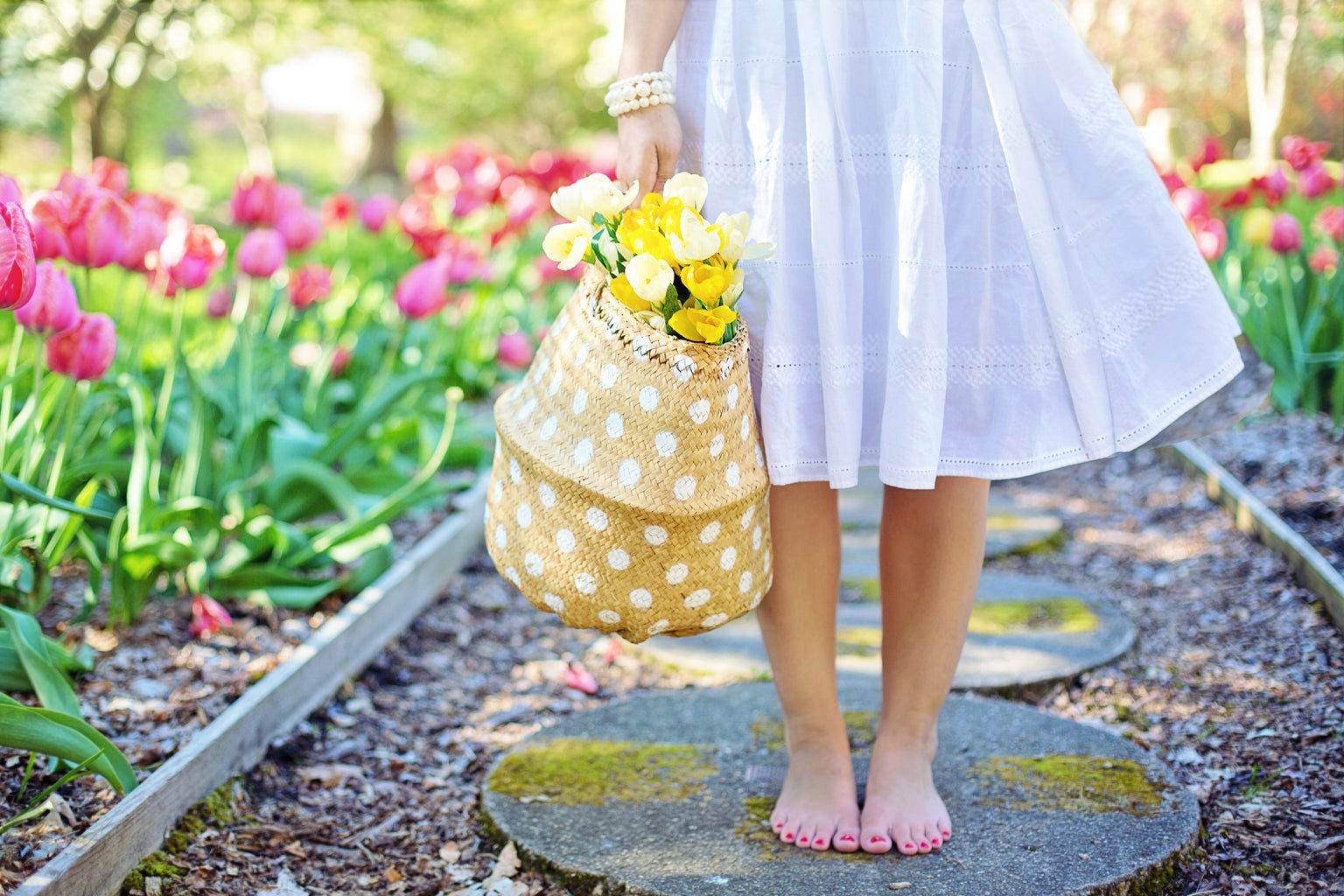 woman staning barefoot in a flower garden holding a basket of yellow flowers