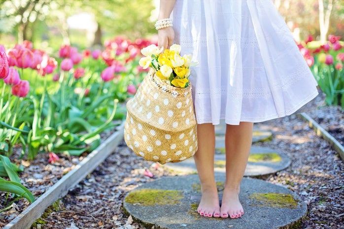 woman staning barefoot in a flower garden holding a basket of yellow flowers