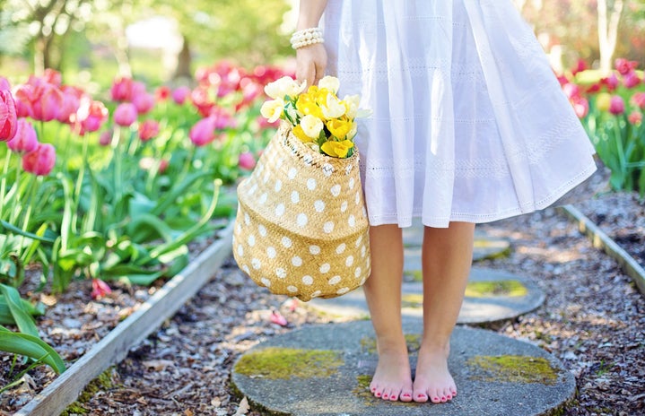 woman staning barefoot in a flower garden holding a basket of yellow flowers