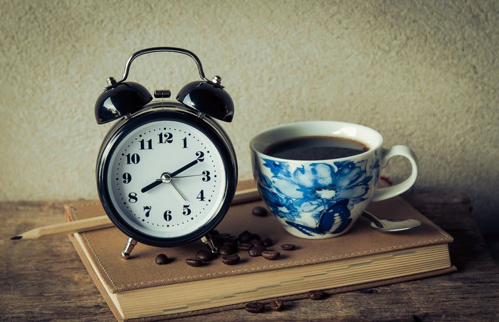 coffee in a blue pattern mug next to an analog alarm clock