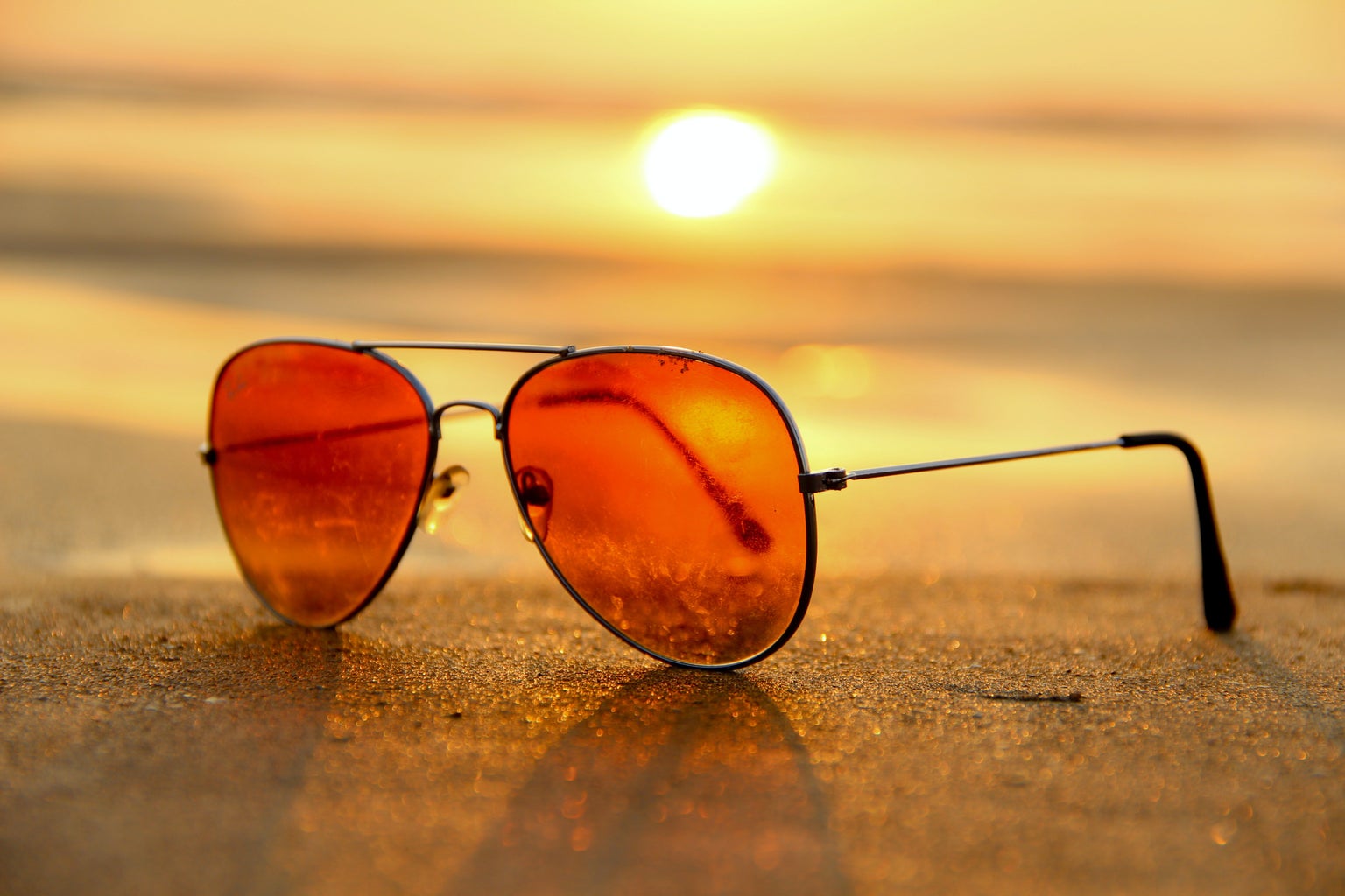 close-up of orange aviator sunglasses on sand at beach