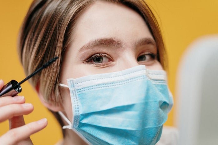 Woman putting on makeup with a face mask on