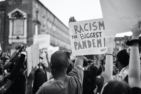person holding a sign that says "racism is the biggest pandemic"