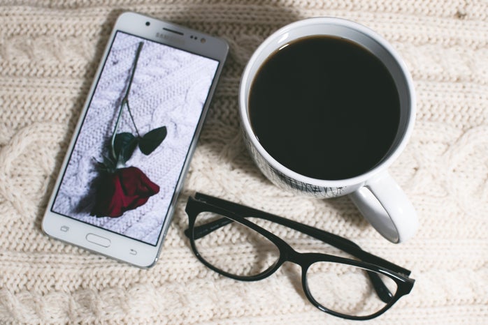 Samsung phone with a rose picture, glasses, mug of coffee on a white textured background
