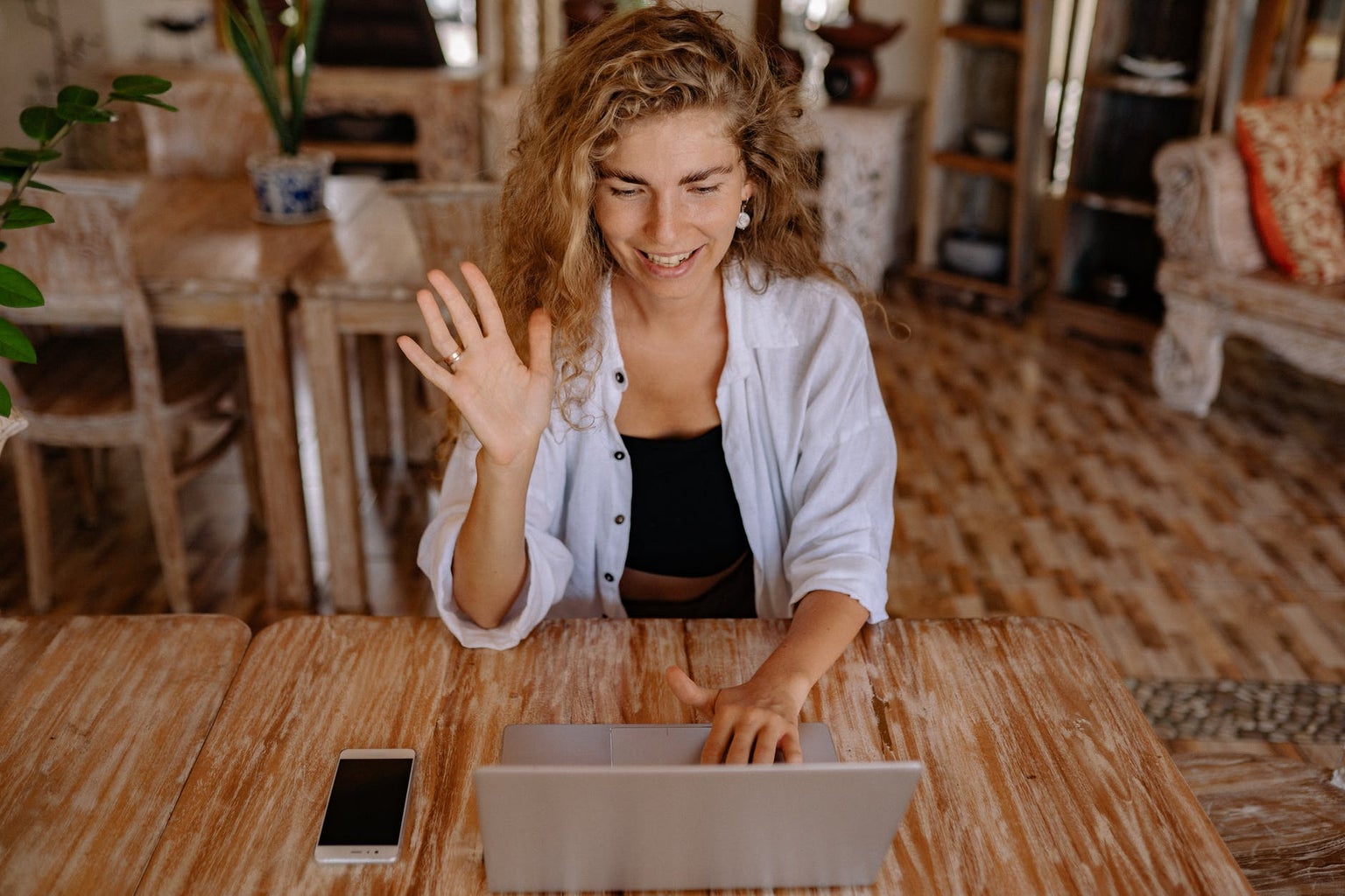 Woman with curly hair waving and saying hi to someone through her laptop.