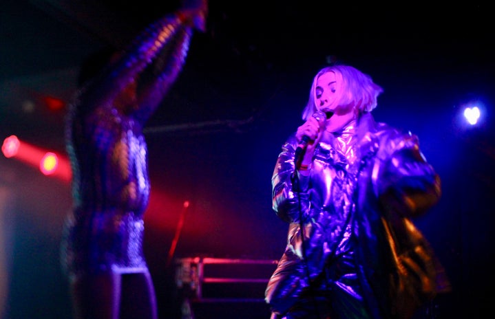 Artist Dorian Electra singing at a live show with a dancer in the background.