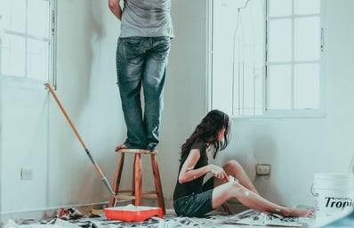 man standing on stool and woman sitting on floor while painting walls in white